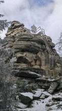 Rock formation with metal stairs in snow surrounded by a wintry sky, Fichtelgebirge