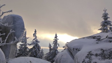 Snowy landscape at dusk with rocks and trees under cloudy sky, Fichtelgebirge
