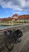 Bicycle on a bridge across a river with historic buildings in the background under cloudy sky,