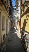 A bicycle is parked in a narrow sunny alley between old buildings, Slovenia