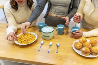 Three young women gather around a wooden table, preparing a morning breakfast with a bowl of