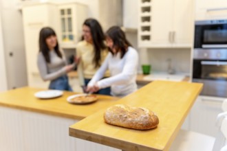 Loaf of artisan bread resting on a wooden kitchen counter while a group of three female friends