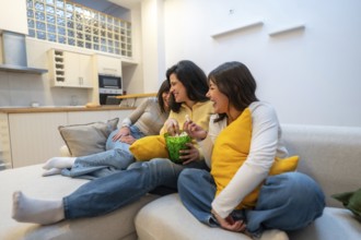 Group of diverse young women enjoying a relaxed evening on the couch at home, sharing laughter and