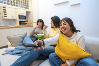 Three young women on a cozy sofa enjoying a movie night, laughing, sharing popcorn and relaxing