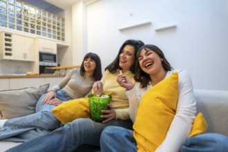 Three young female friends sitting on a sofa in a modern apartment, enjoying an entertaining movie