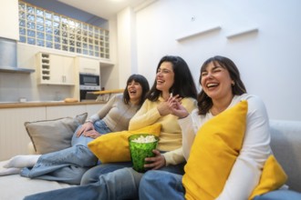 Three young adult female friends enjoying a relaxing movie night at home, laughing together,