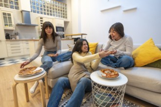 Three young women lounging on a sofa and floor, sharing pizza, laughing and chatting in a cozy