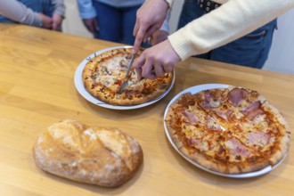 Person's hands using a knife and fork to cut a hot pizza into slices, ready for sharing a casual