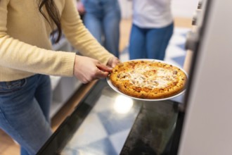 Person pulls a freshly baked pizza from the oven, hands ready to serve a hot, cheesy slice to
