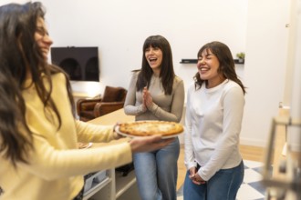 Group of female friends laughing and joyfully anticipating a hot pizza during a casual home