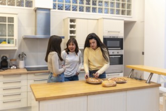 Three young women in a modern kitchen preparing homemade pizza, chatting and laughing while bonding