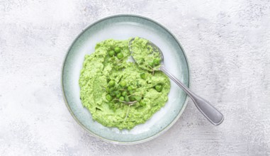 A vibrant green pea puree fills a shallow bowl, topped with fresh peas and microgreens. The dish