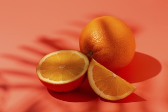 On the coral surface, next to two neatly sliced slices, there is a whole orange. Sunlight casts