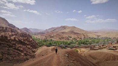 A hiker enjoys the view of a barren mountain landscape with a village in the distance, Morocco