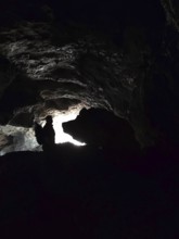 Silhouette of a person in a dark cave entrance with a ray of light from outside and a rock that