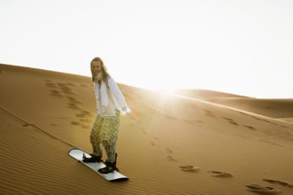 Young woman with snowboard in the sand dunes, near Merzouga, Meknès-Tafilalet region, Erg Chebbi,