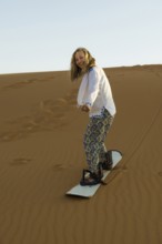 Young woman with snowboard in the sand dunes, near Merzouga, Meknès-Tafilalet region, Erg Chebbi,