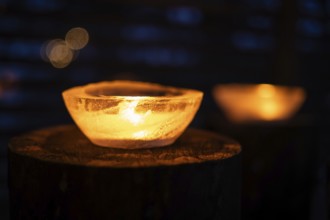 Ice bowls illuminated by burning tea lights stand on tree trunks, winter, Finland