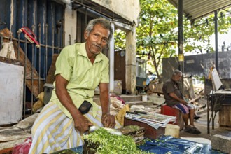 Elderly man cuts vegetables at a street market in an urban setting