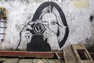 Black and white wall painting of a woman with camera in an urban environment