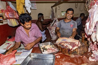 Butcher working with fresh meat, one smiles and works on a large block of wood