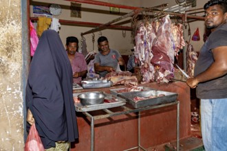 A butcher market with sellers and customers looking at and buying pieces of meat