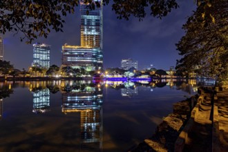 A calm lake reflects an illuminated skyline and urban buildings at night, The Seema Malaka Temple