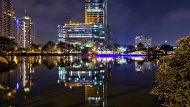 At night, illuminated modern buildings and a temple are reflected in the tranquil lake, The Seema