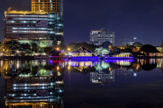 At night, an illuminated temple and urban skyline are reflected in the water, The Seema Malaka