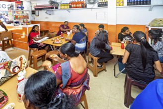 A busy restaurant where people sit at tables and talk, people in a simple restaurant in Colombo in