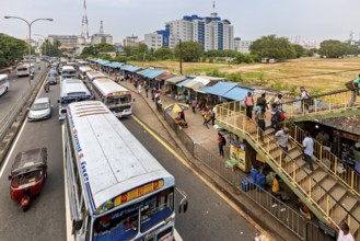 City street with buses and busy market on the right, buildings in the background, buses on the road
