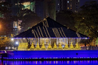 A temple shrouded in lights with golden Buddha statues at night, The Seema Malaka Temple in Colombo