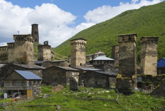 Medieval stone towers and buildings in front of a wooded mountain and cloudy sky, defensive towers,