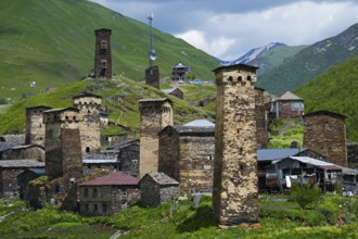 Historic mountain village with distinctive stone towers surrounded by green hills under a cloudy