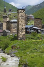 Mountain village with old stone towers on a river, nestled in a green alpine environment, defensive