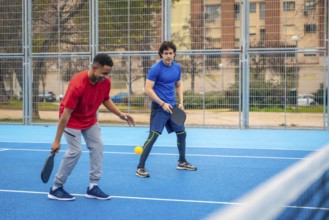 Two diverse young men compete on a blue outdoor pickleball court, focused and energetic as they