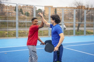 Two smiling male athletes, one african american and one caucasian, giving a high five on a blue