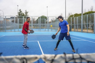 Two young men playing pickleball, hitting the ball over the net during a competitive match on an