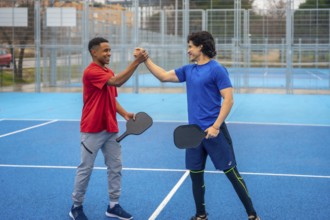 Two smiling male pickleball players of different ethnicities shaking hands on a vibrant blue court