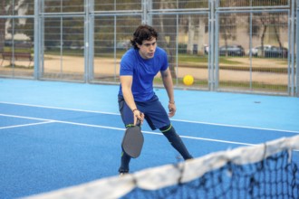 Young man concentrating on a pickleball match on a blue outdoor court, holding his paddle ready to