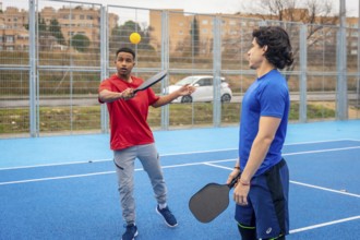 Young men enjoying a game of pickleball, one hitting the ball with a paddle on a vibrant blue