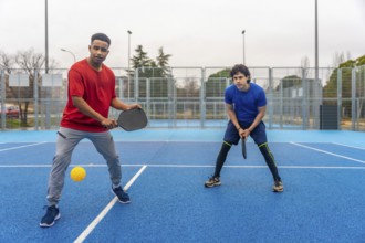Two young men actively engaged in a pickleball game on an outdoor blue court, holding rackets and