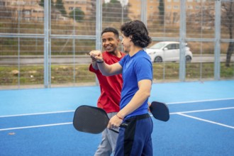Two diverse male athletes fist bumping on an outdoor blue pickleball court, symbolizing
