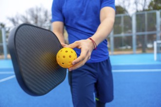 Athlete preparing for a game, holding a perforated yellow pickleball and a black paddle on a blue