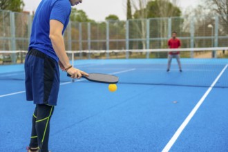 Player serving during a competitive pickleball match on a vibrant blue outdoor court, ready to hit