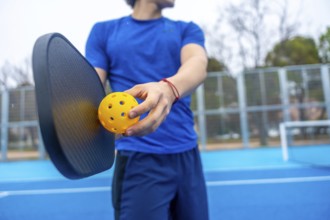 Athlete preparing to serve, holding a yellow pickleball and paddle on a vibrant blue outdoor court,