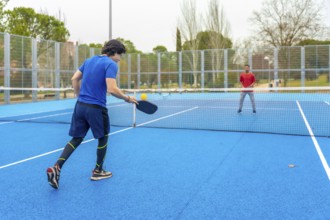 Two male athletes playing an intense pickleball game on a vibrant blue court, hitting the ball over