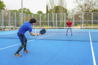 Two young men actively engaging in a game of pickleball, one hitting the yellow ball with a paddle,
