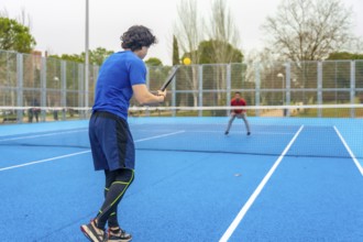Two young men engaging in a spirited game of pickleball on a vibrant blue outdoor court, focused on