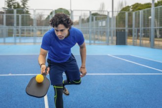 Male athlete concentrating while holding a pickleball paddle and yellow ball, ready to serve or